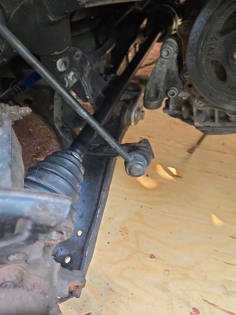 Close-up view of a car's suspension components, including a driveshaft with a rubber boot and various metal brackets and joints, on a wooden surface.