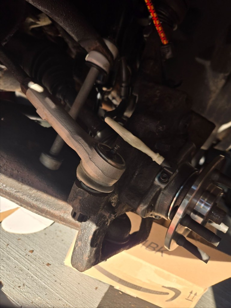 Close-up of a mechanical component under a vehicle, showcasing steering and suspension parts, with visible bolts and connectors.