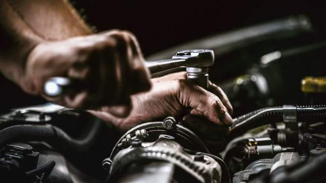 Close-up of a mechanic's hand using a wrench on a car engine, illustrating mobile automotive repair services.