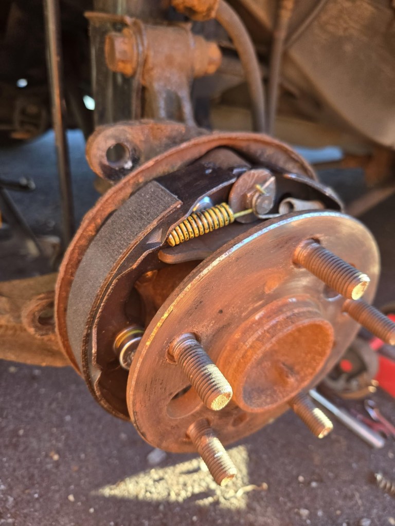 Close-up view of a brake drum assembly showing the brake shoes, springs, and fastening hardware in an automotive repair setting.