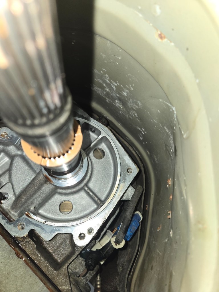 Close-up view of a mechanical component, showing a steel rod connected to a metallic gearbox, with visible electrical wiring and a cylindrical housing.